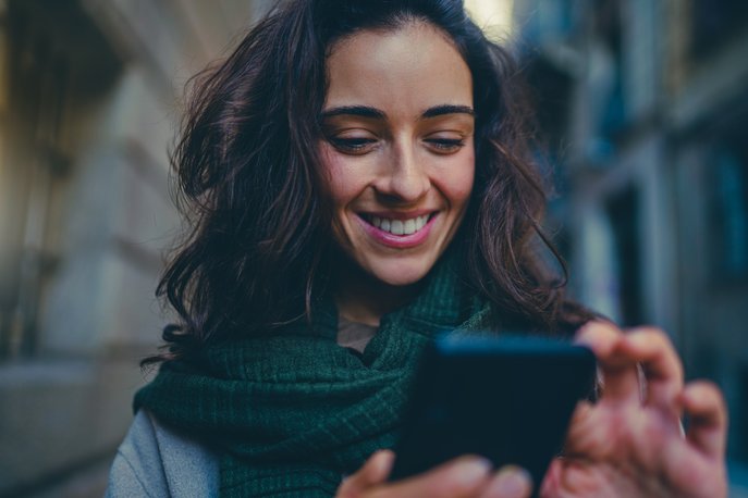 Kvinde, der smiler til telefonen, viser, hvor nemt det er at bruge appen APCOA FLOW til at finde en parkeringsplads